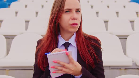 Young Woman with Notepad Pen Sitting on Stadium Bleachers Alone