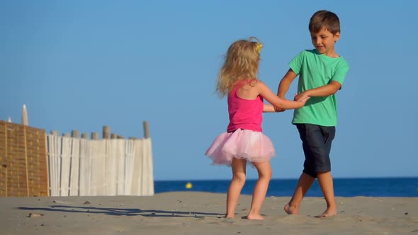 Little Boy and Girl in the Pink Skirt are Dancing on the Beach