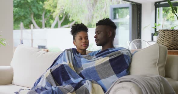 Video of happy african american couple sitting on sofa with blanket