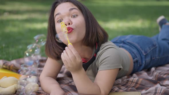 Positive Little Woman Blowing Soap Bubbles Lying in Spring Park Outdoors Smiling