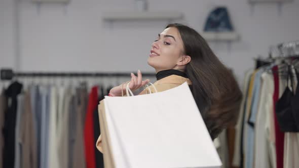 Beautiful Slim Caucasian Millennial Woman Turning Hanging Shopping Bags on Shoulder Looking at