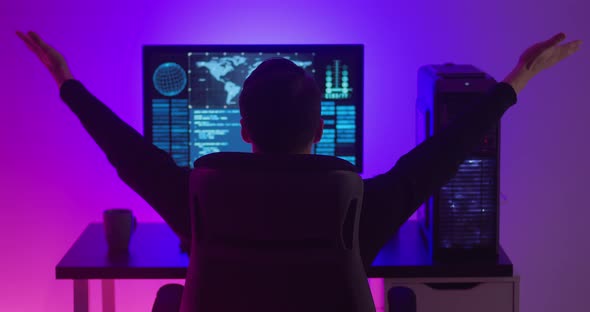 Rear View of Man Programmer Happy with Success While Working at a Computer in Data Center at Night