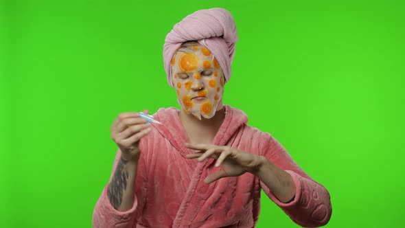 Young Man in Bathrobe with Face Mask Painting His Hand Nails