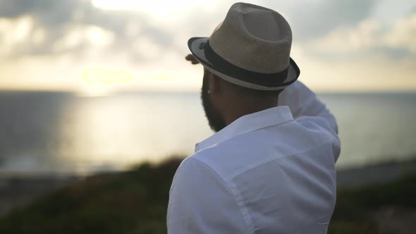 Male African American Tourist in Hat and White Shirt Looking at Sunrays at Sunset Standing on