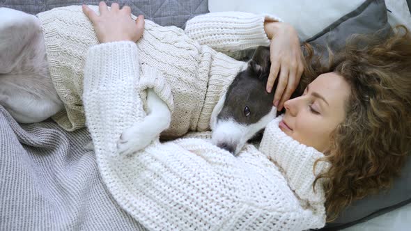 Young Woman Lying And Sleeping With Dog In Bed Wearing Cozy Knitwear