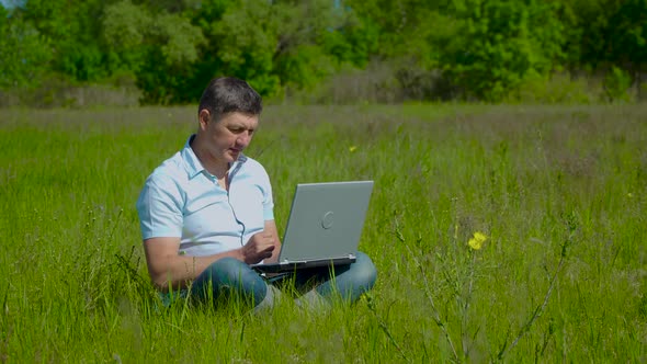 Businessman Works Behind a Laptop Sitting on the Grass