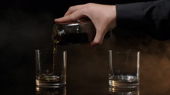 Barman Pour Golden Whiskey Cognac Brandy Bourbon Rum From Bottle Into Glasses on Dark Background