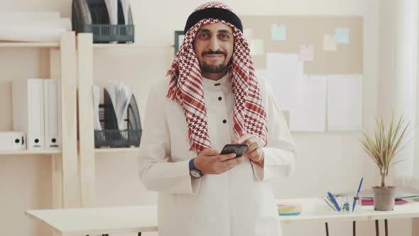 The Sheikh in Kufiyeh Looks at Phone, Looks at the Camera, and Nods. The Arab Businessman at the
