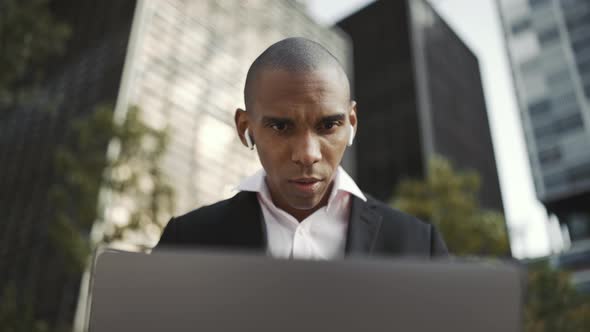 Serious African businessman working on laptop and talking in headphones