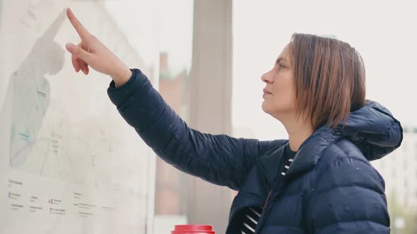 A Young Adult Woman Examines the Schedule and Route of Buses