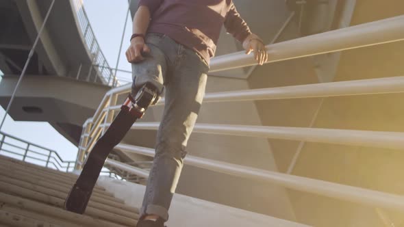 Handsome Man with Leg Prosthesis Stands on Steps at Sunset