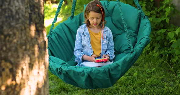 A Little Girl the on Hanging Chair Outdoors Play Pop It Kid Hands Playing