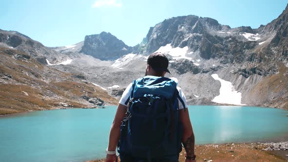 A young climber with a large hiking backpack goes to a mountain lake in summer