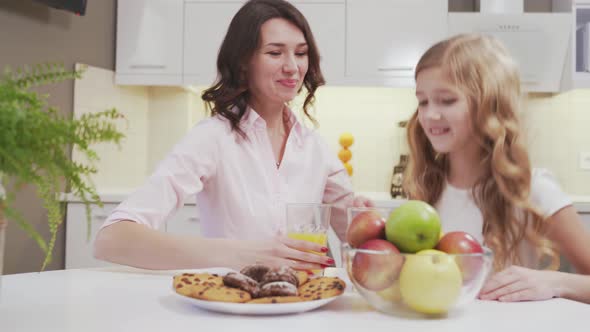 Little Girl and Charming Woman Sitting at Table in Kitchen