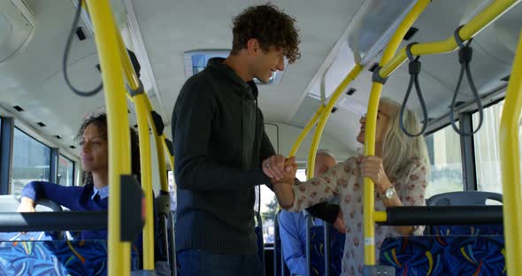 Male commuter helping mature commuter to get up while travelling in bus 4k