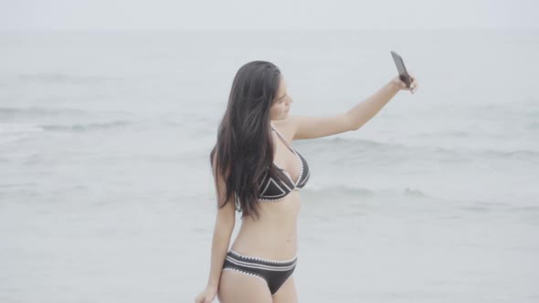 Beautiful young asian woman in bikini sexy taking photo with smartphone on the beach for leisure.