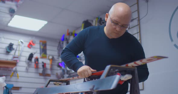 Professional Craftsman with Glasses Removes an Unnecessary Layer From the Surface of the Skis with a