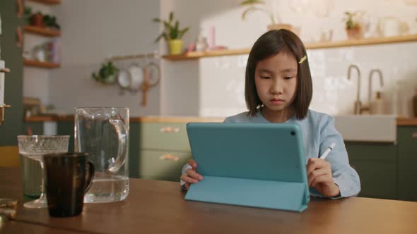 Curious Asian Preschool Kid Girl Using Digital Tablet Technology Device Sitting By Desk Alone