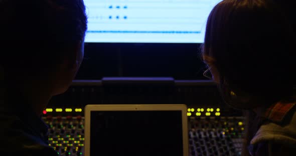 Audio engineers using laptop while mixing sound