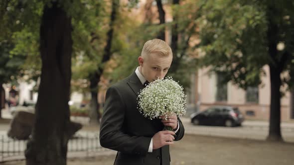 Groom Standing at the Park Alley with a Wedding Bouquet Waiting to His Beloved Bride First Meeting