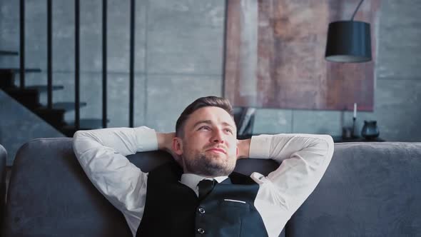 Handsome Man European Appearance Classic Clothes White Shirt Sits in Stylish Dark Office on Couch