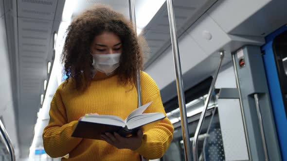 Young Dark Skinned Female Rides the Subway and Reads a Book a Student in a Medical Mask Goes to