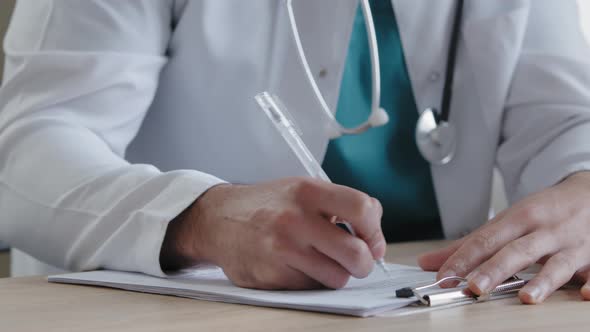 Unknown Man Doctor Young Male Therapist in White Uniform Sit at Clinic Desk Write Detailed