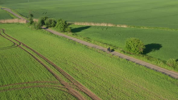 Motorcyclist Moves on Narrow Ground Pathway Between Fields