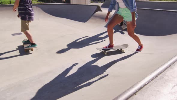 Low section of caucasian woman and two male friends skateboarding on sunny day