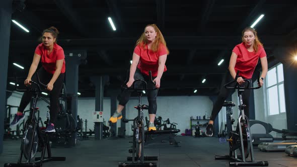 Group Athletic Girls Performing Aerobic Riding Training Exercises on Cycling Stationary Bike in Gym