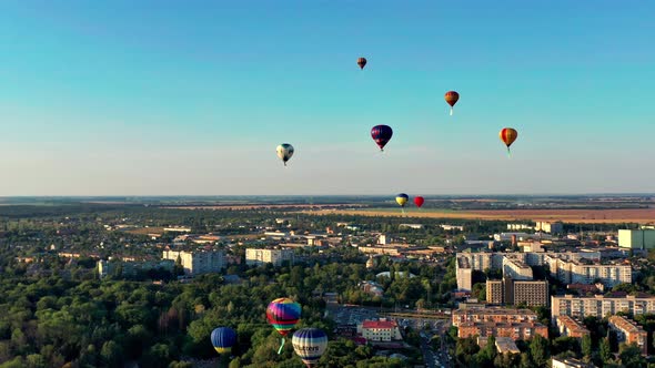 Multicolored balloons fly over fields, houses, trees. Blue sky.