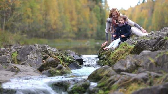 A Young Mother and Her Cute Daughter Sitting Near the Forest Stream