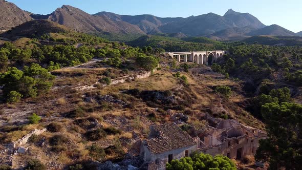 Flying over the ruins of an old stone house, with an arched bridge in the background