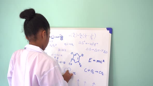 African American Girl in Lab Coat Drawing Mathematic and Science Formulas on White Board