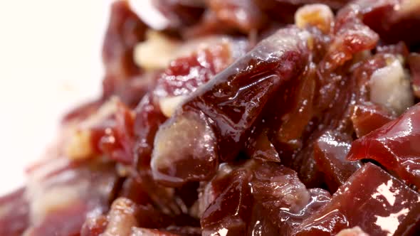 Fatty prosciutto pieces rotating on white surface, macro shot in 4k. Extreme close up view.