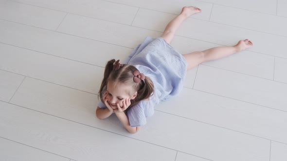 Little girl in a blue dress is lying on the floor in the bedroom. Children's products