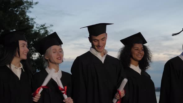 Happy Smiled Mixed Races Graduates Walking with the Diplomas in Hands.