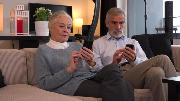 An Elderly Couple Sits on A Couch in An Apartment and Each Works on Their Smartphone