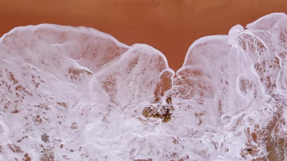 Waves Crashing on Rock surrounded by Red Sand in Ferragudo, Portugal, Aerial