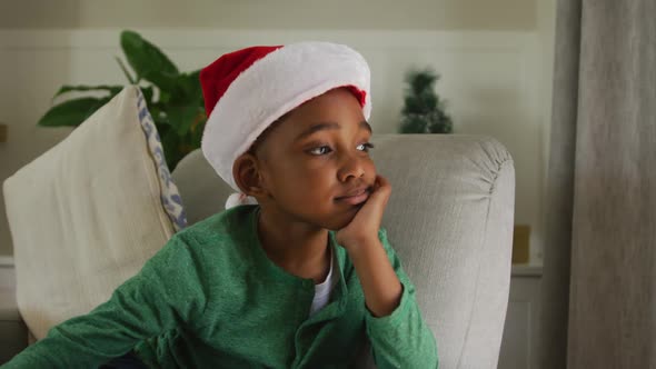 Animation of sad african american boy wearing santa hat sitting on sofa at christmas time