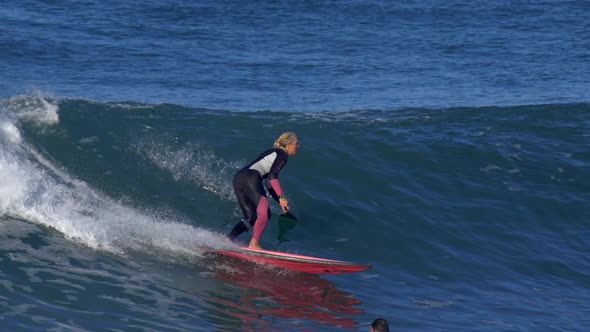 A woman rides an sup stand up paddleboard while surfing on a pink surfboard