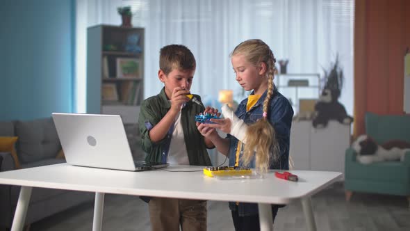 Children Repair a Mini Quadcopter with Tools and Then Give Each Other Five Girl with Plaster Cast on