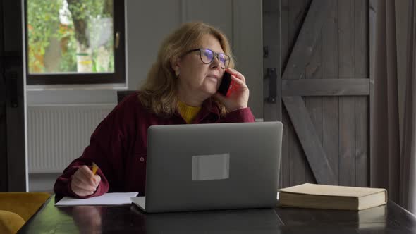 senior woman talking by phone and using laptop computer at home.