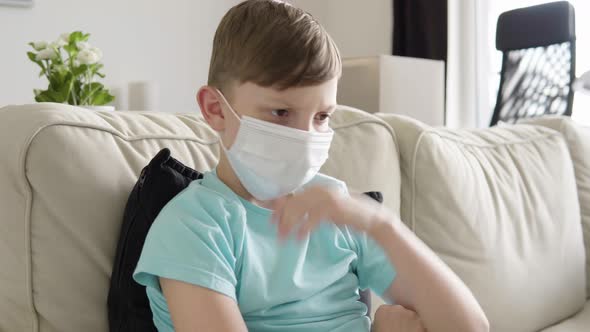 A Young Boy in a Face Mask Acts Upset As He Sits on a Couch at Home - Closeup