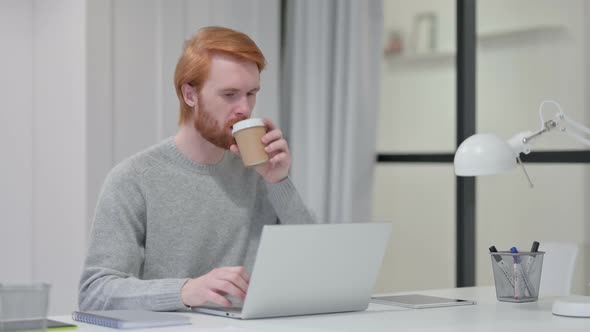 Beard Redhead Man Drinking Coffee While Typing on Laptop