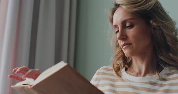 Female Student Reads a Book in a Cozy Bright Living Room Sitting on a Sofa