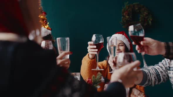Over Shoulder View of Woman Sitting at Family Table in Christmas Hat Clinking Glass of Champagne
