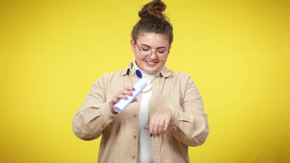 Smiling Caucasian Plussize Woman Applying and Smelling Hand Moisturizer at Yellow Background