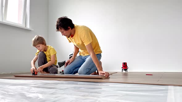 Father and His Little Son Install Laminate on the Floor in Their Apartment