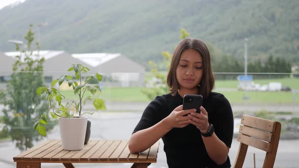 Attractive Thai woman using her phone on the balcony in the city, urban garden